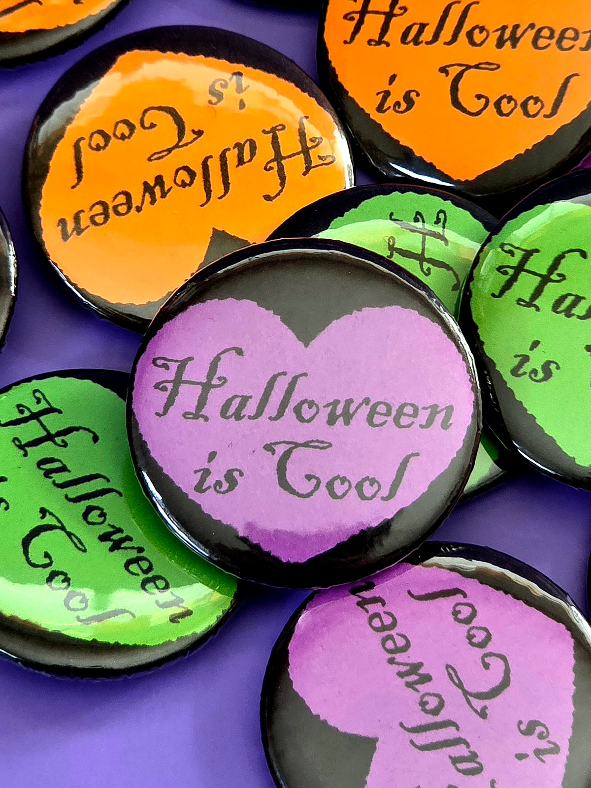 a purple button that says "Halloween is cool" with a black heart around it
