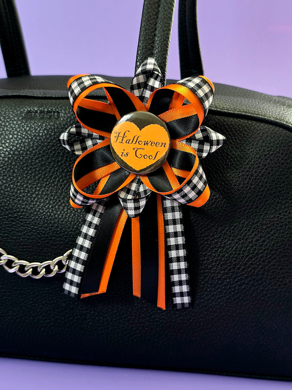 Prize ribbon made with blac, orange, and checkered black and white ribbon has an orange button in the center that says "Halloween is cool". It is attached to a bag.