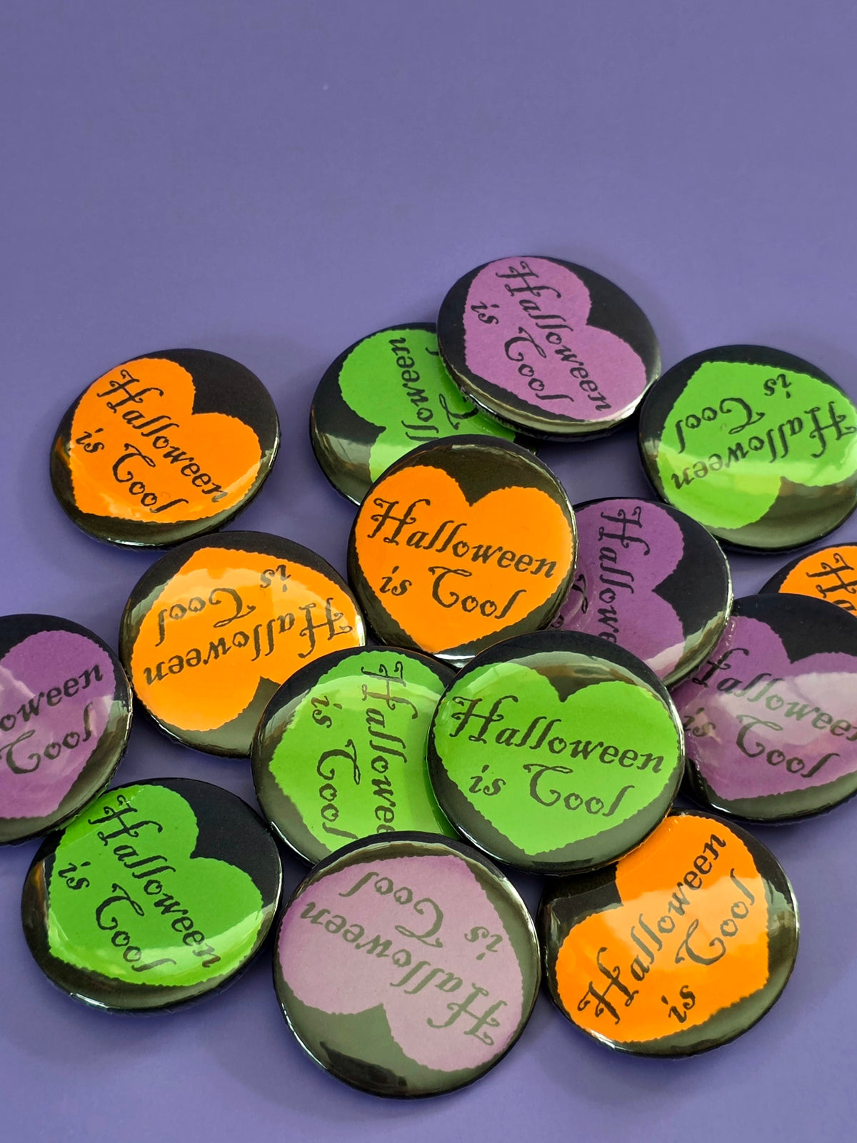 a pile of buttons that say "Halloween is cool" with a black heart around the words.