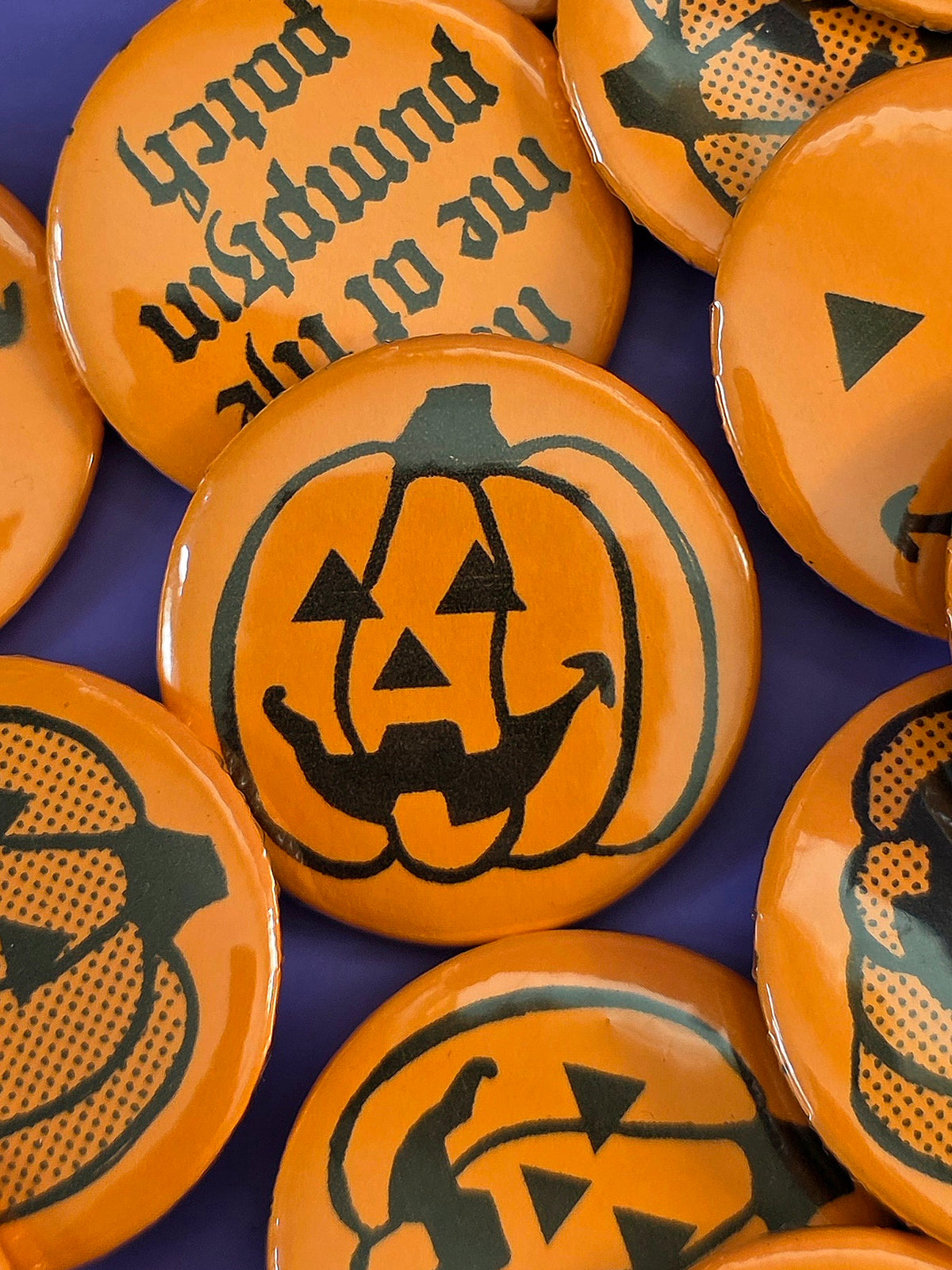 a round, orange pin back button with a jack-o'-lantern design on the front