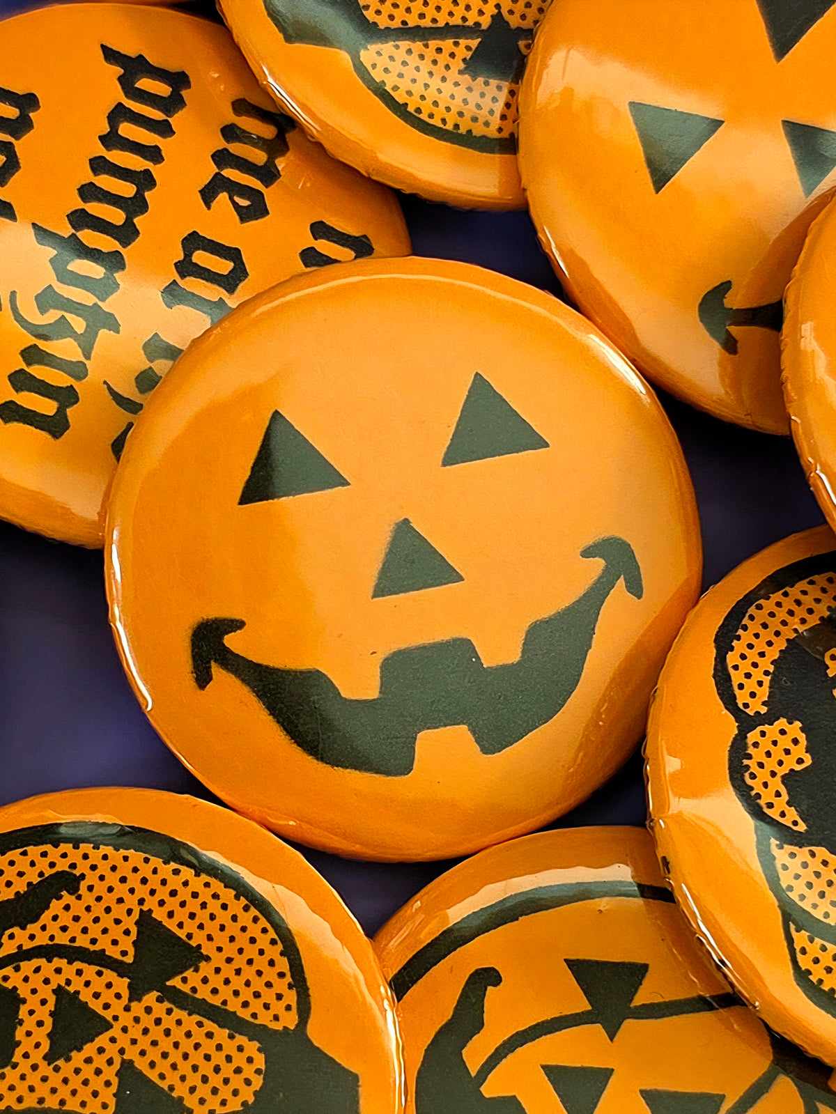 a round, orange pin back button with a jack-o'-lantern face design on the front