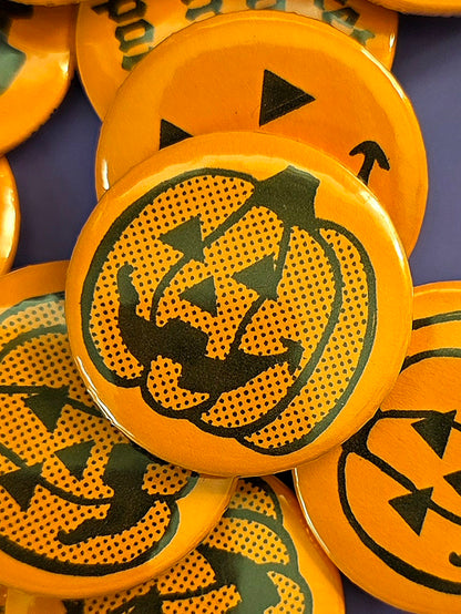 a round, orange pin back button with a jack-o'-lantern design with halftone dots on the front