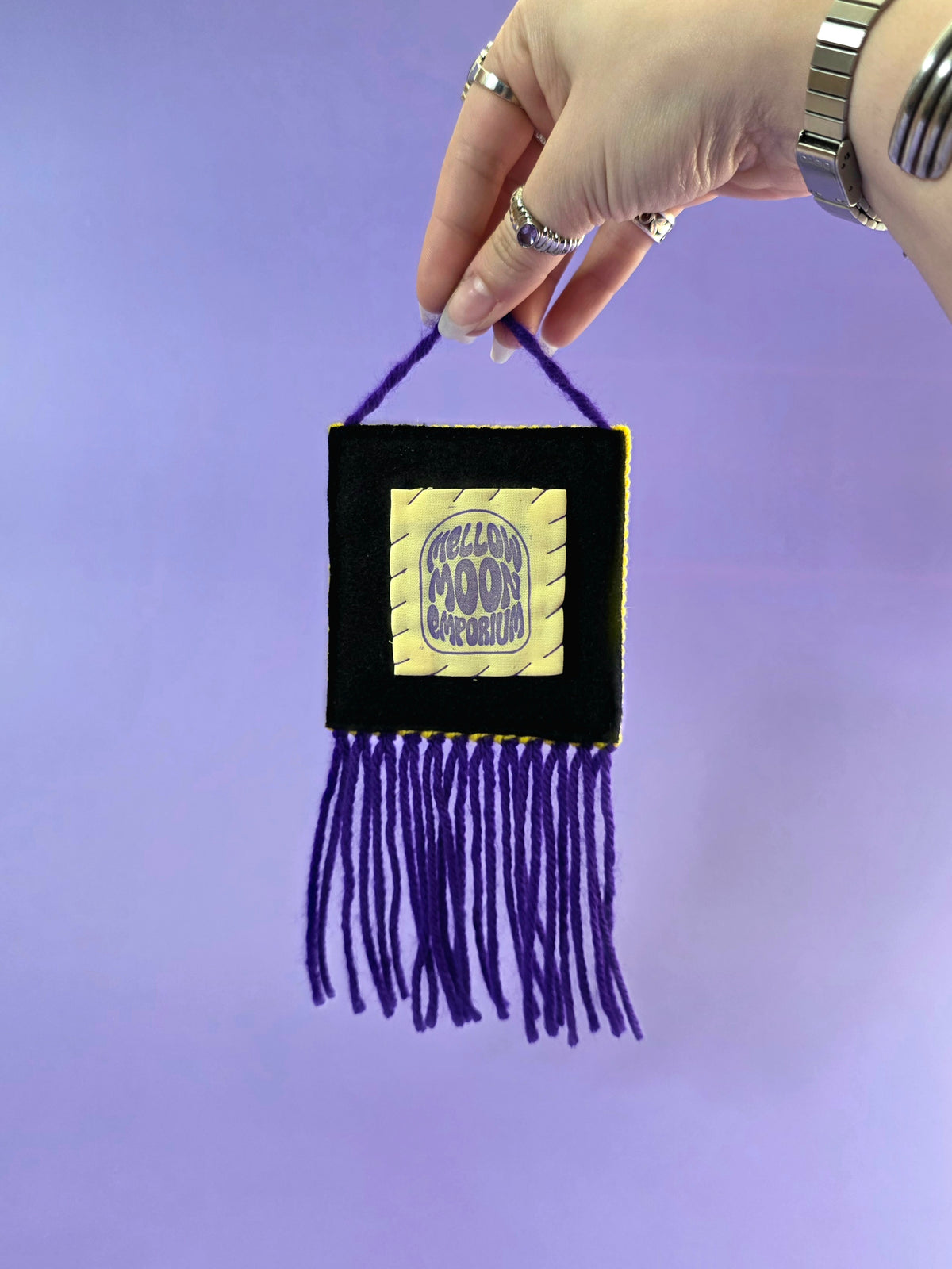 the back of the wall hanging has a yellow and purple label that says mellow moon emporium. it is hand sewn onto black premium felt.