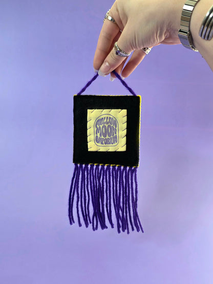 the back of the wall hanging has a yellow and purple label that says mellow moon emporium. it is hand sewn onto black premium felt.