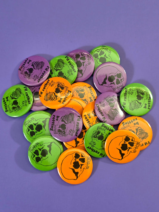 a pile of buttons, some say "I'd rather be rotting" with  skull with heart eyes and fungi coming out of it and some just have skulls  with heart eyes on them